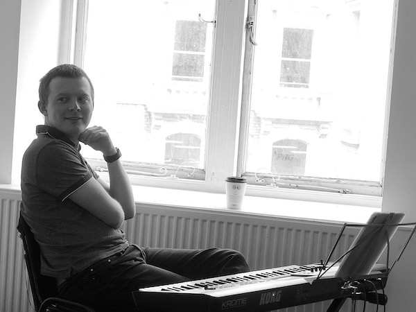 A black and white image of Josh. He is sitting behind a keyboard looking into the distance
